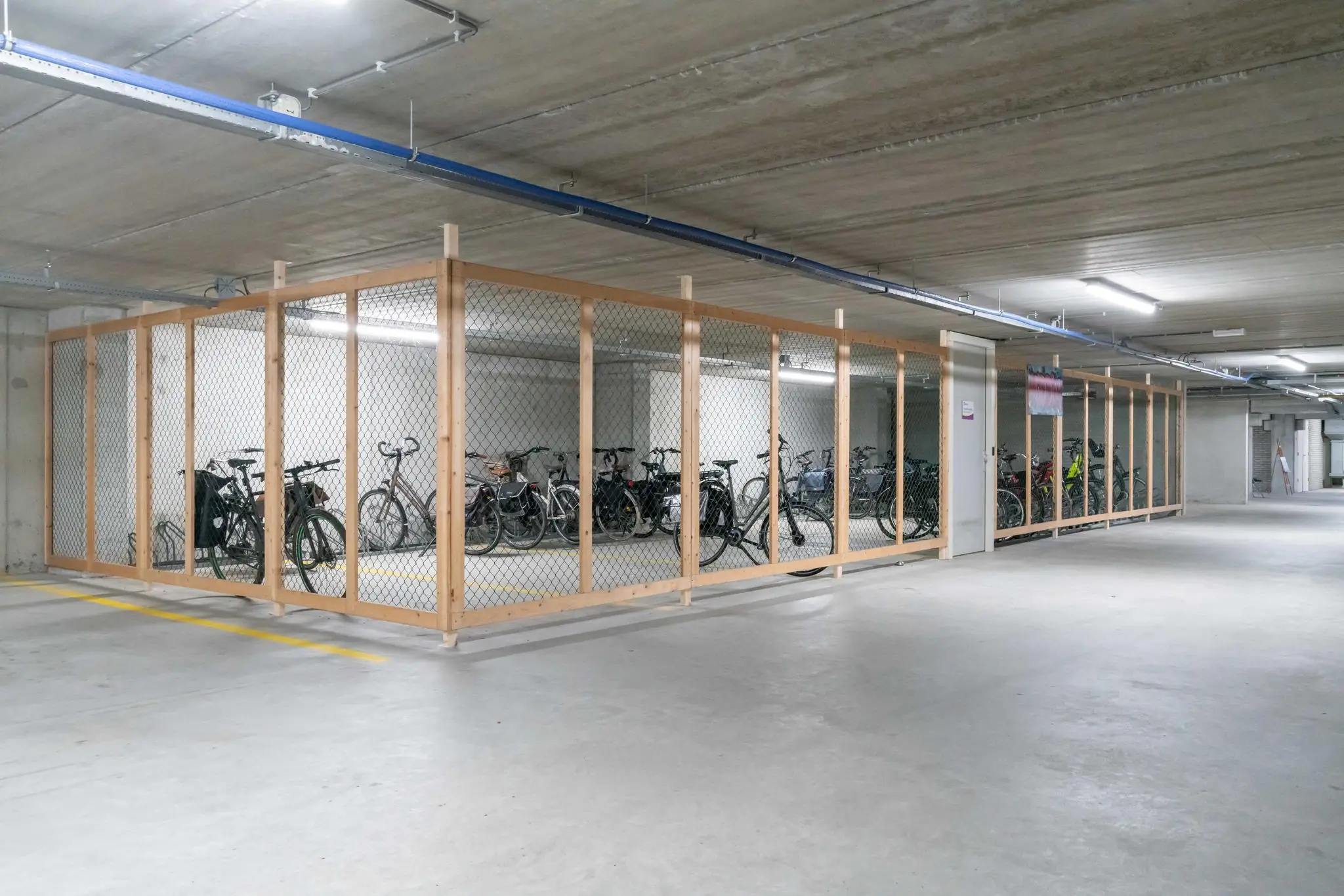 Afgesloten fietsenstalling met houten frame en gaaswerk in een ondergrondse parkeergarage aan de De Bruyn Kopsstraat.